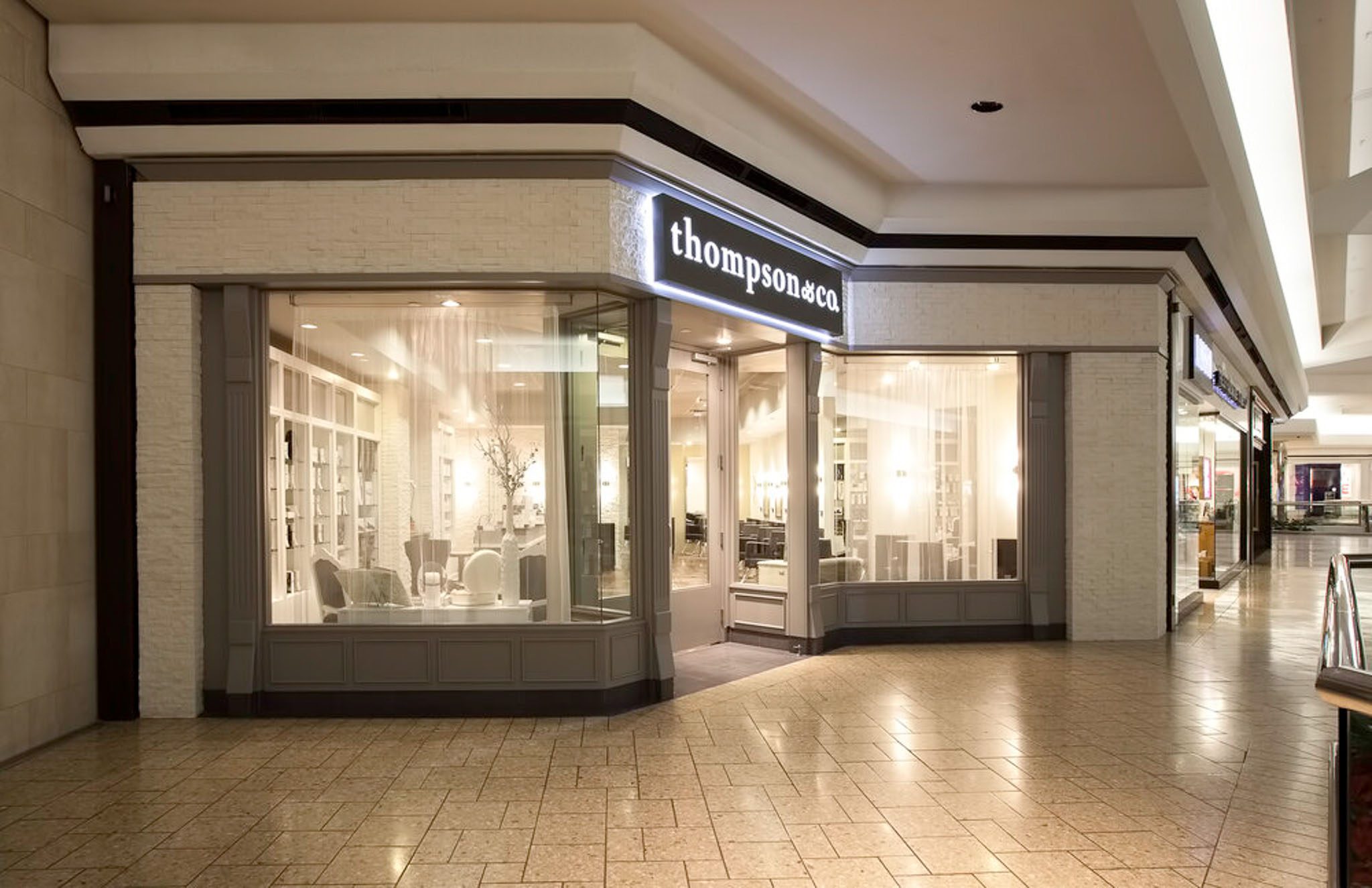 Storefront of "thompson & co" in a mall, with large glass windows displaying interior with styled hair products and salon chairs.