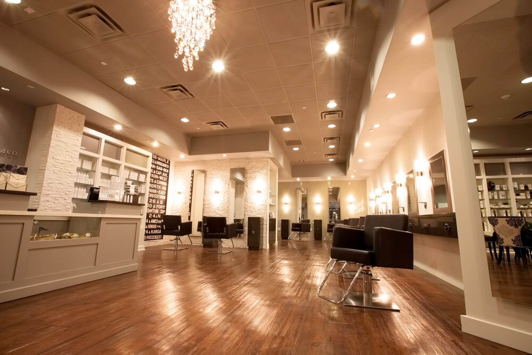 A modern hair salon interior with wooden flooring, salon chairs, mirrors, and a chandelier.