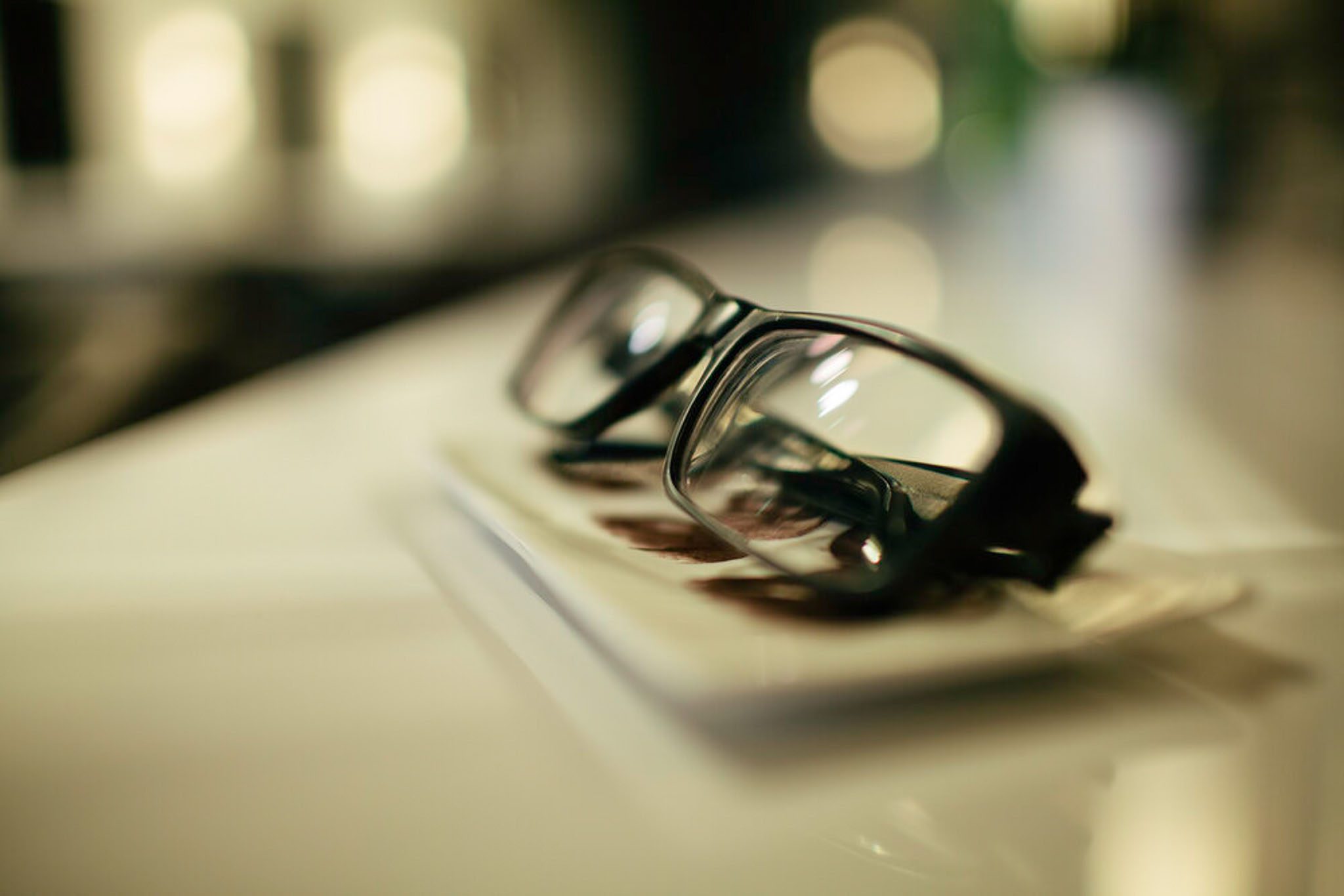 A pair of black-rimmed glasses resting on a closed book with a blurred background.