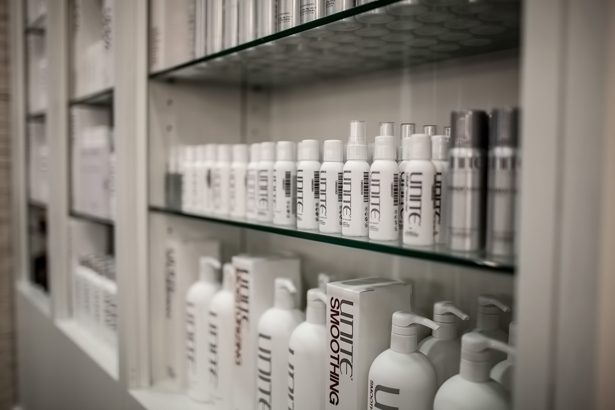 A display shelf with various bottles of Unite hair products, including shampoos and sprays, lined up neatly behind a glass case.