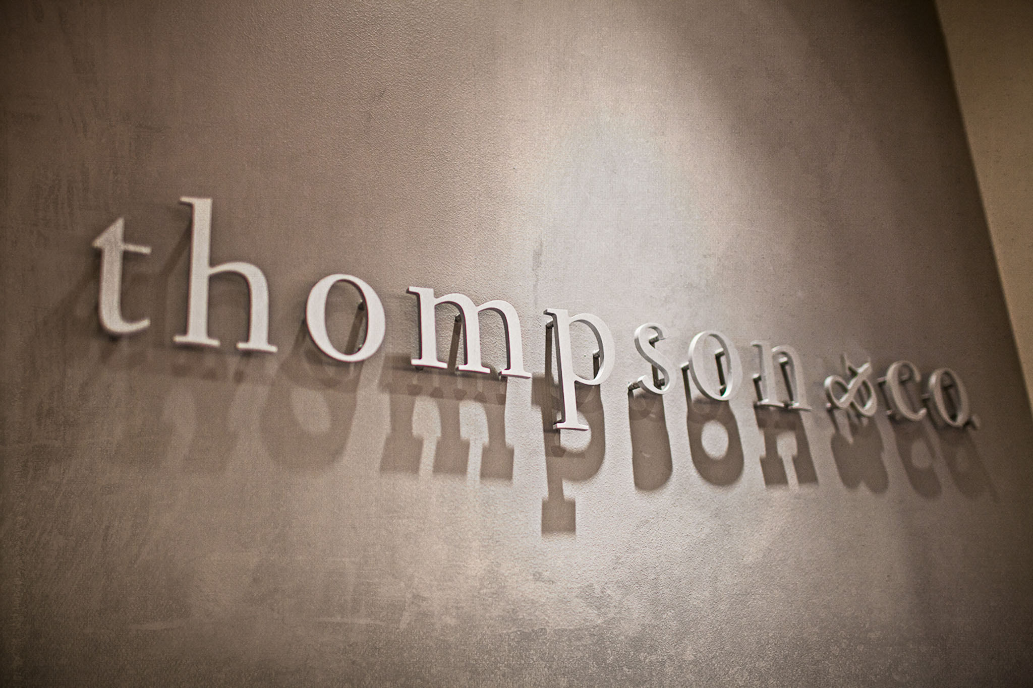 Silver lettering on a wall spelling "thompson co" with cast shadows.
