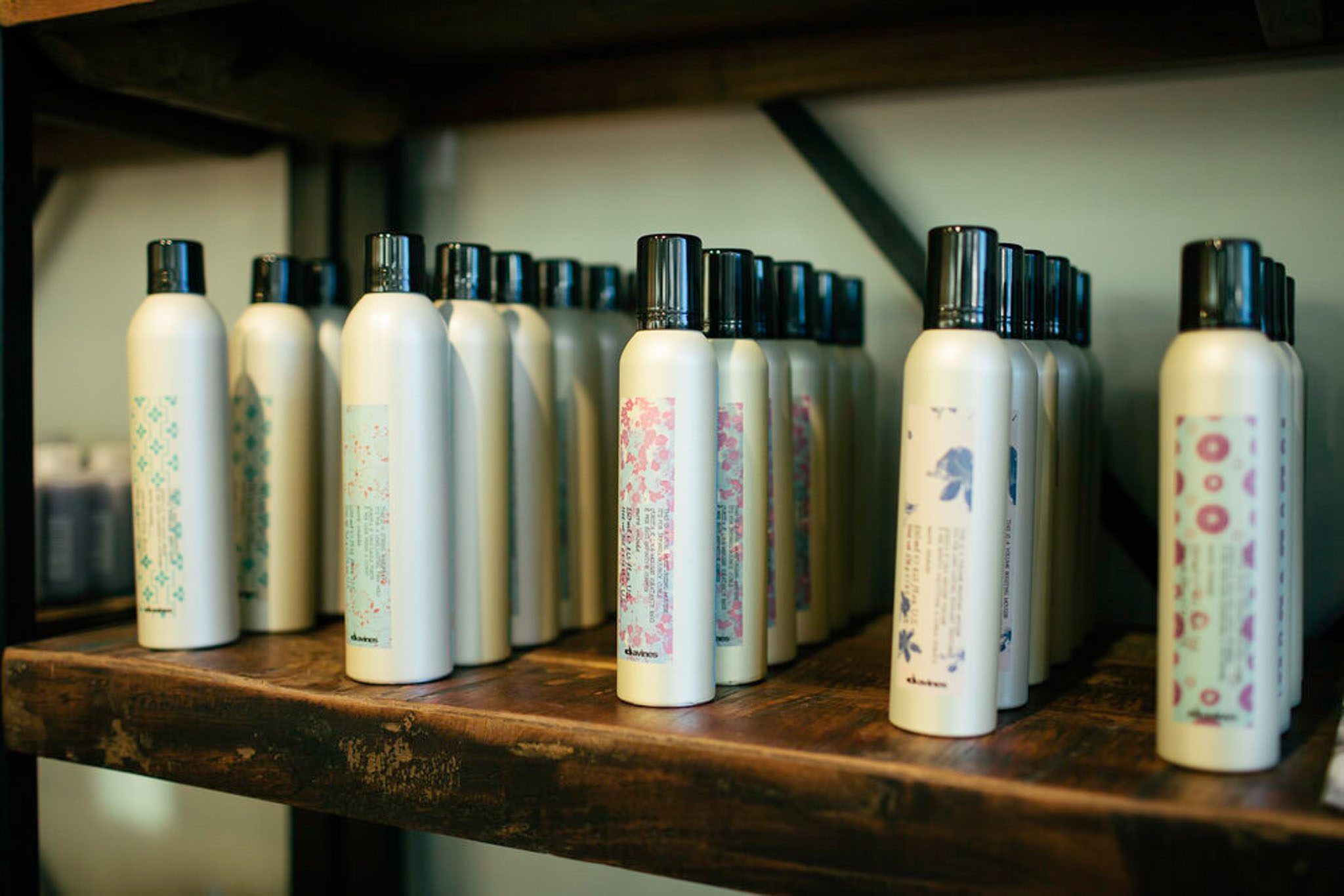 Several white bottles with black caps, displaying various floral designs, are arranged on wooden shelves.