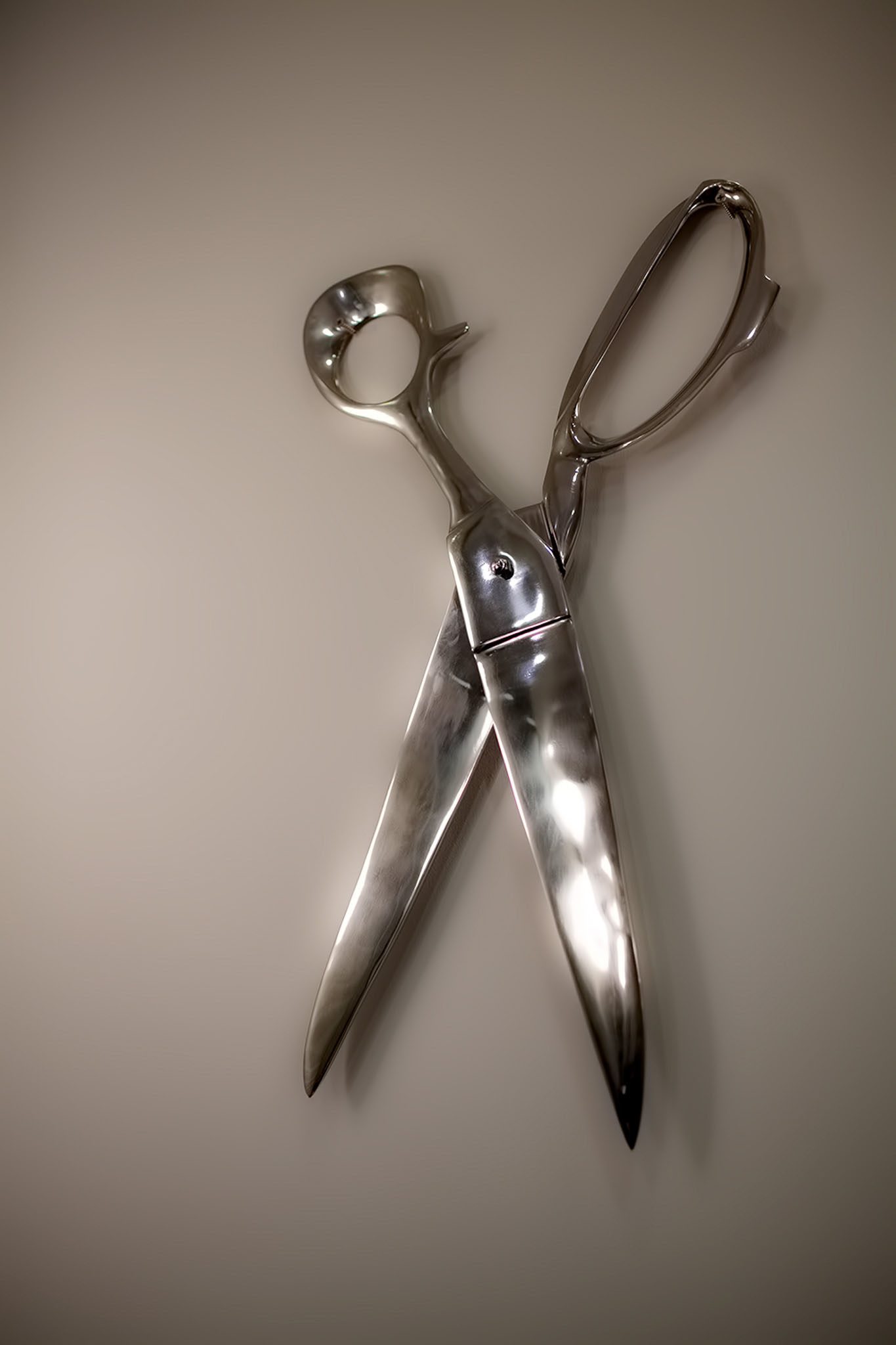 A large, metallic pair of scissors displayed in an open position against a plain background.