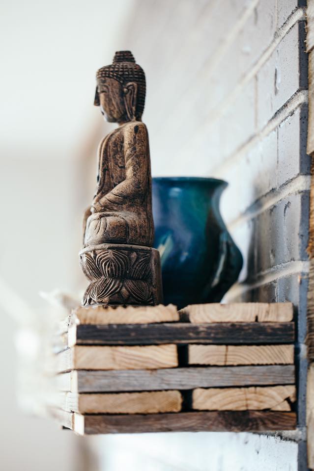 Wooden Buddha statue sitting on a stack of wooden planks with a blue-green bowl in the background.