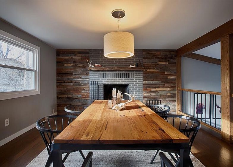 Dining room with a large wooden table, six black chairs, a modern pendant light, and a fireplace with a reclaimed wood accent wall.