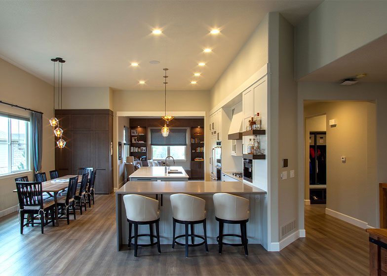 Modern open-concept kitchen and dining area with pendant lighting, wood floors, a large island with stools, and a dining table near a window.